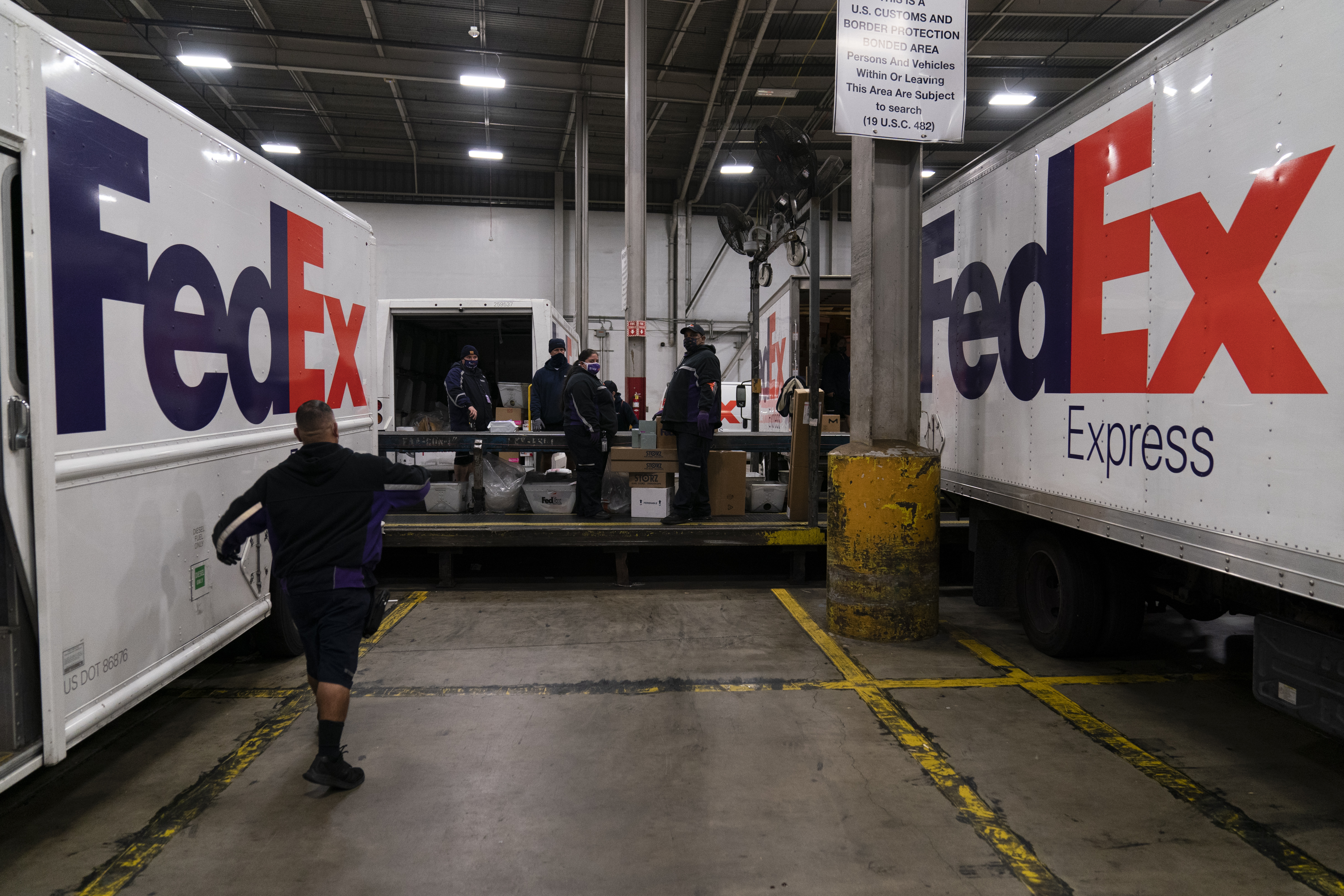FILE - FedEx delivery trucks are parked next to a conveyor belt while being loaded with...